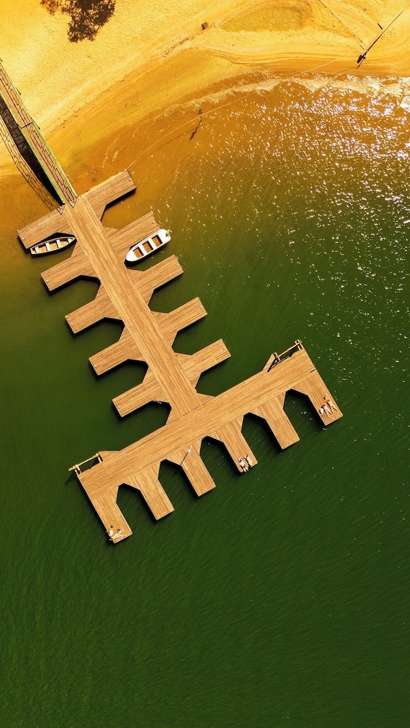 An aerial view of a wooden pier extending into a body of water, with a small boat docked at one end.