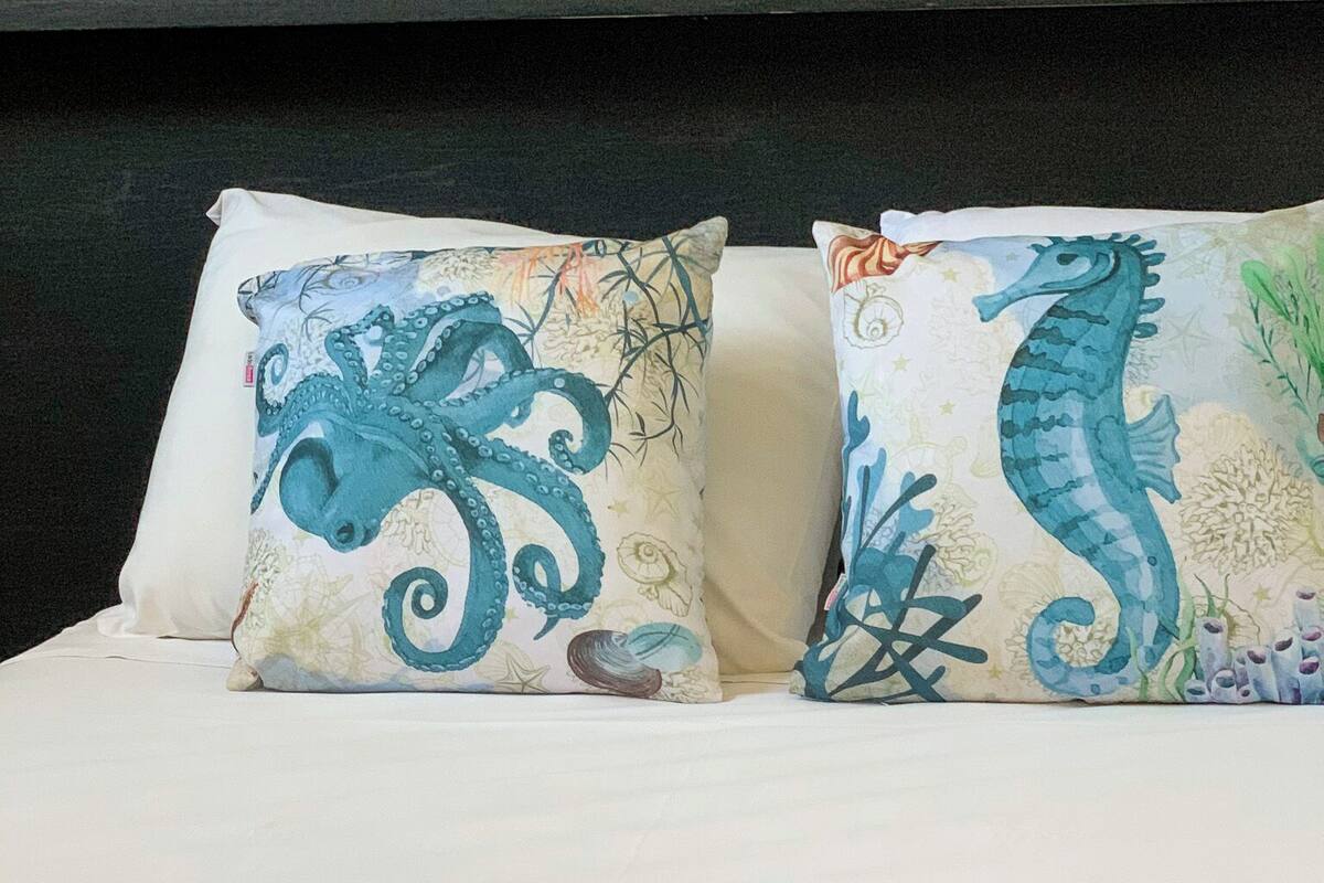Un lit agrémenté de deux coussins décoratifs représentant des créatures marines, une serviette blanche soigneusement pliée et une tête de lit sombre.