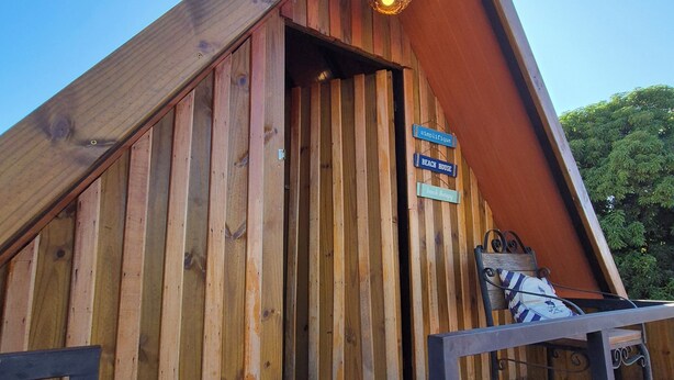 A wooden cabin with a sloped roof, a wooden deck, and a sign indicating it is a beach house. - Pousada & Restaurante Praeros LTDA (Rifaina)