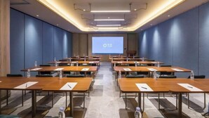 Egy konferenciaterem, amelyben több asztal, szék és egy nagy kivetítő található az elülső falon.