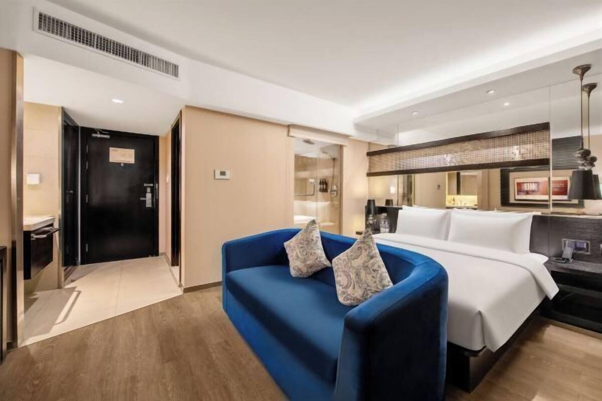 Ein Hotelzimmer mit einem blauen Sofa, einem Bett, einem Schreibtisch und einem Spiegel.