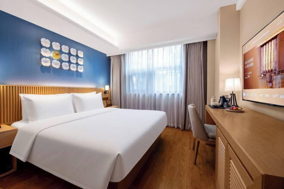 Ein Hotelzimmer mit Bett, Schreibtisch, Sessel, Fernseher und einer Wand mit floralem Dekor.