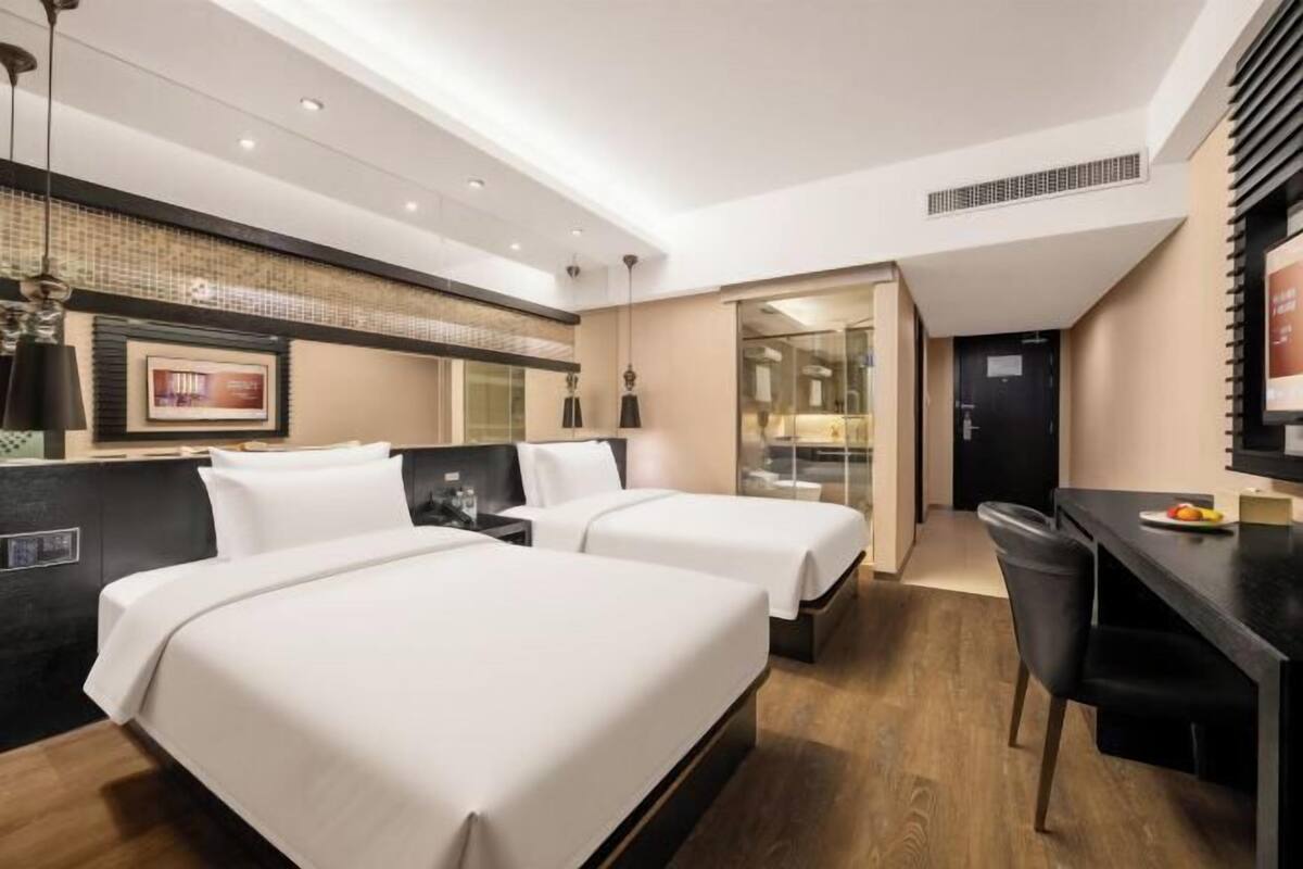 Ein Hotelzimmer mit zwei Betten, einem Schreibtisch, einem Stuhl, einem Fernseher und einem Badezimmer.