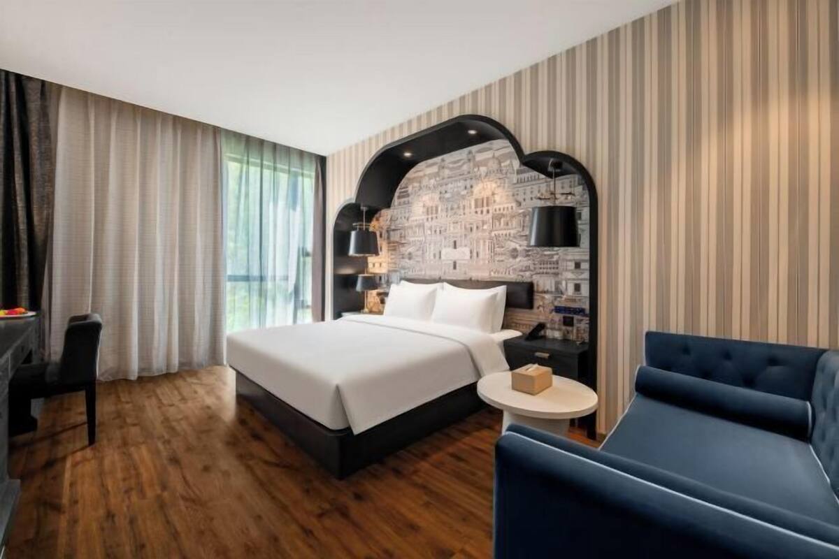 Ein modernes Hotelzimmer mit einem großen Bett, einem runden Beistelltisch, einem blauen Sofa und einer Wandmalerei mit Stadtansicht.