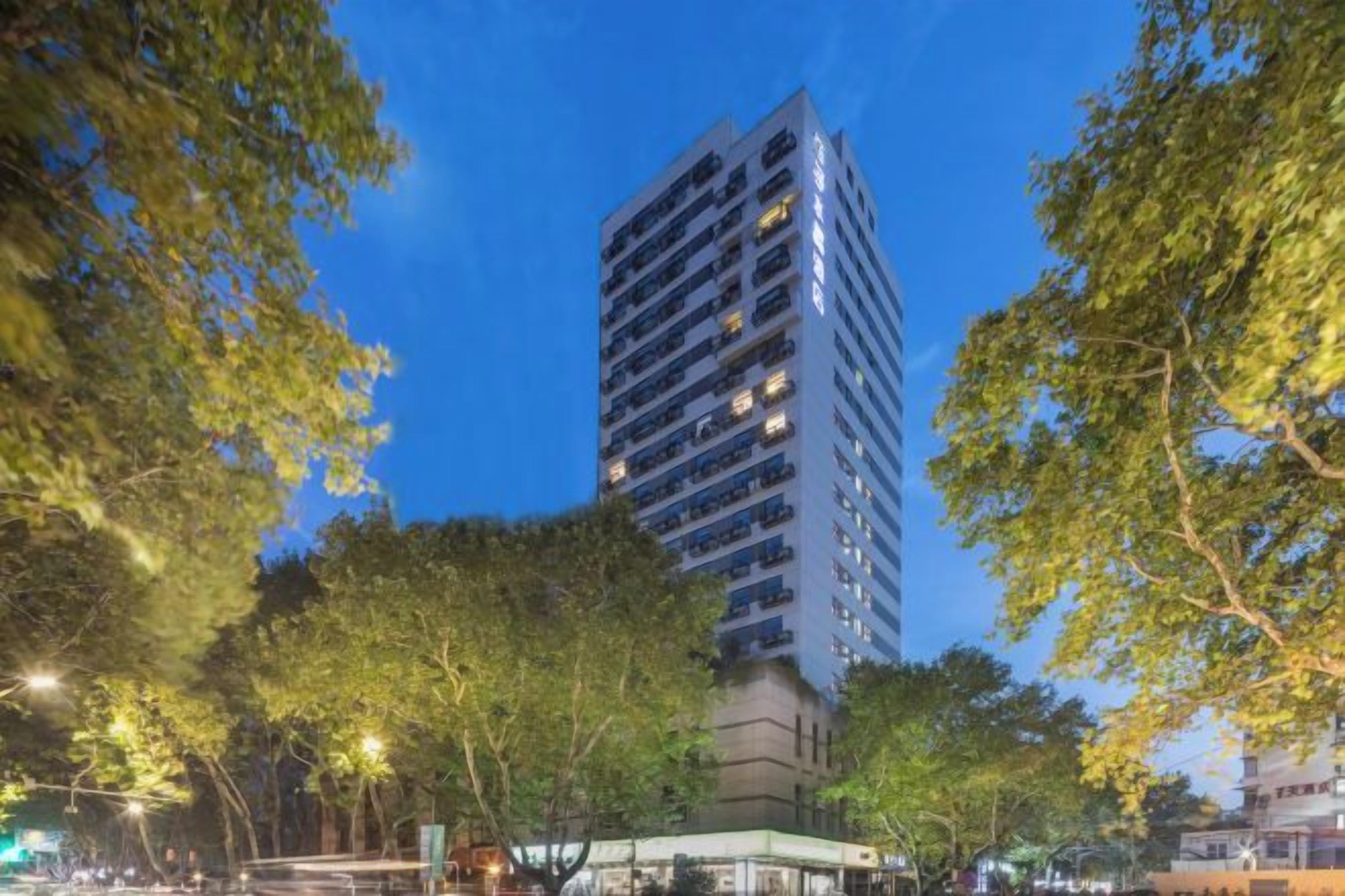 Un edifici alt amb diverses plantes, envoltat d'arbres i fanals.