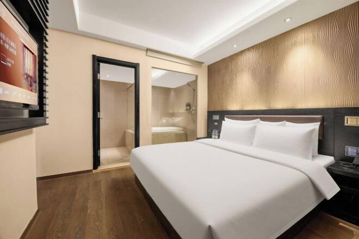 Ein Hotelzimmer mit einem großen Bett, Holzboden, einem Spiegel und einem am Wand montierten Fernseher.