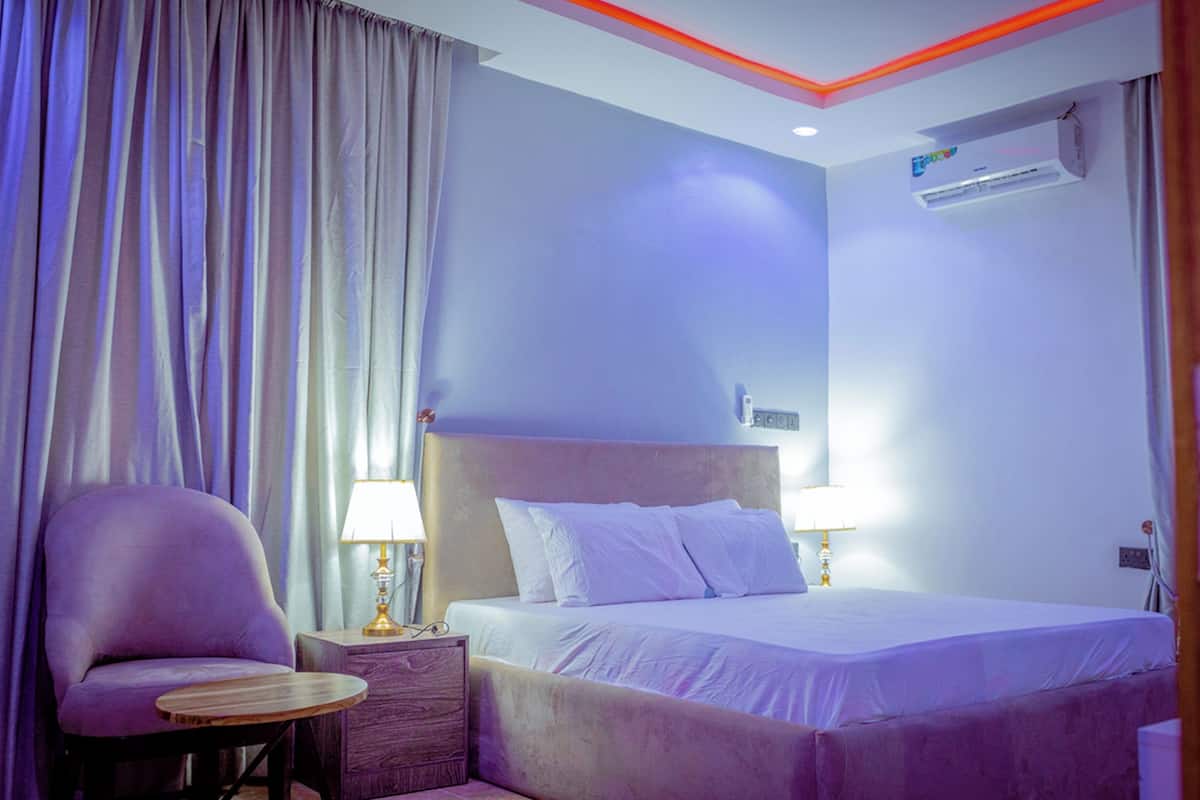 A hotel room with a bed, a chair, a nightstand, and a lamp.