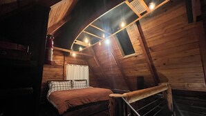 Un dormitorio acogedor en el ático con cama, una ventana pequeña y una escalera de madera.