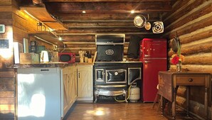 Una cocina rústica con paredes de madera, un refrigerador blanco, una estufa roja y una mesa de comedor de madera.
