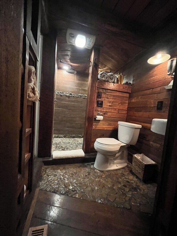 Ein rustikales Badezimmer aus Holz mit einer Steindusche, Toilette und Waschbecken.