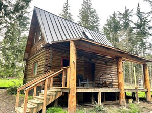 Eine rustikale Blockhütte mit Metalldach, Holzveranda und einer Treppe zum Eingang.