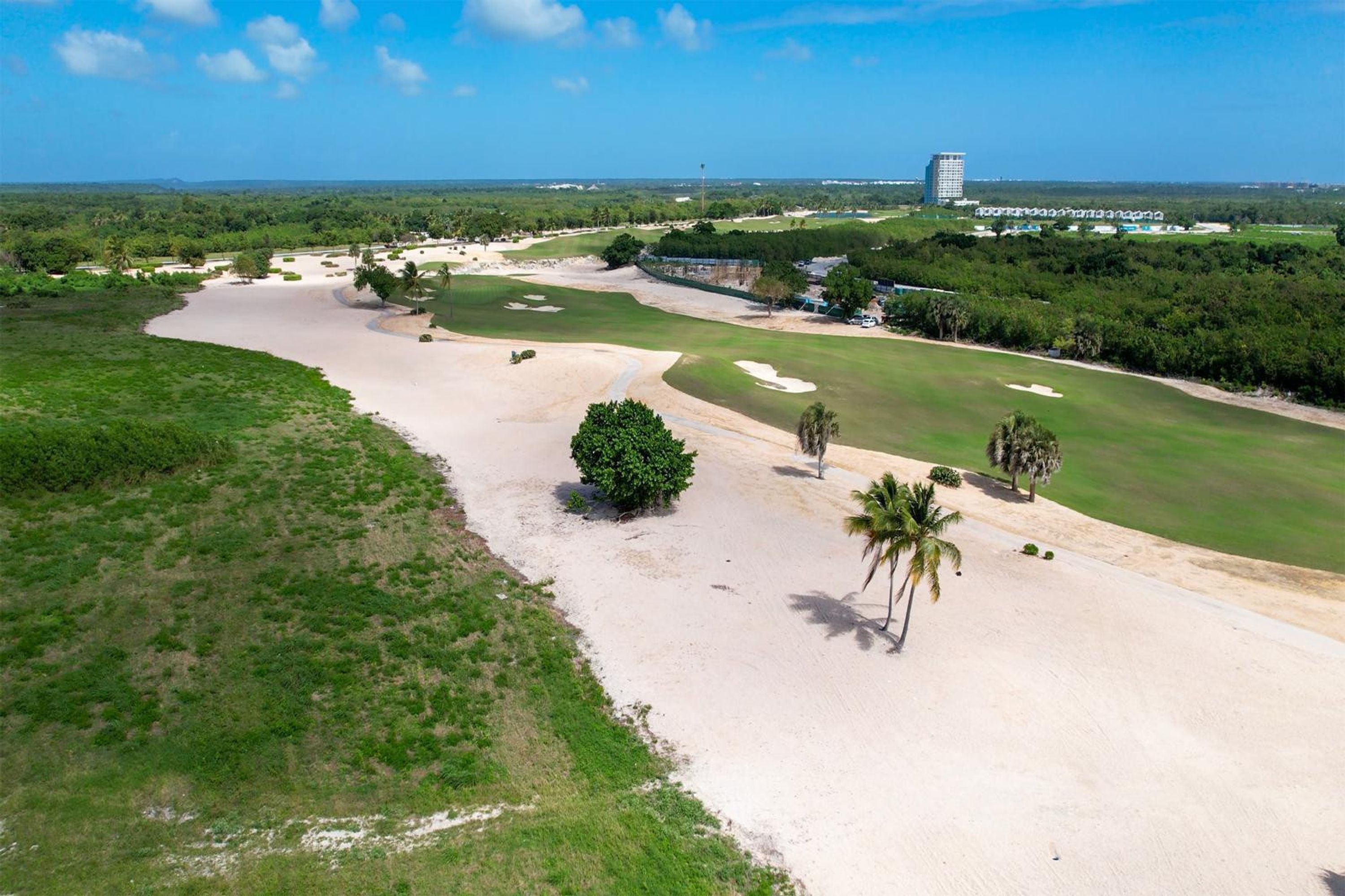 An aerial view of a golf course with sand bunkers, a water hazard, and a building in the distance.