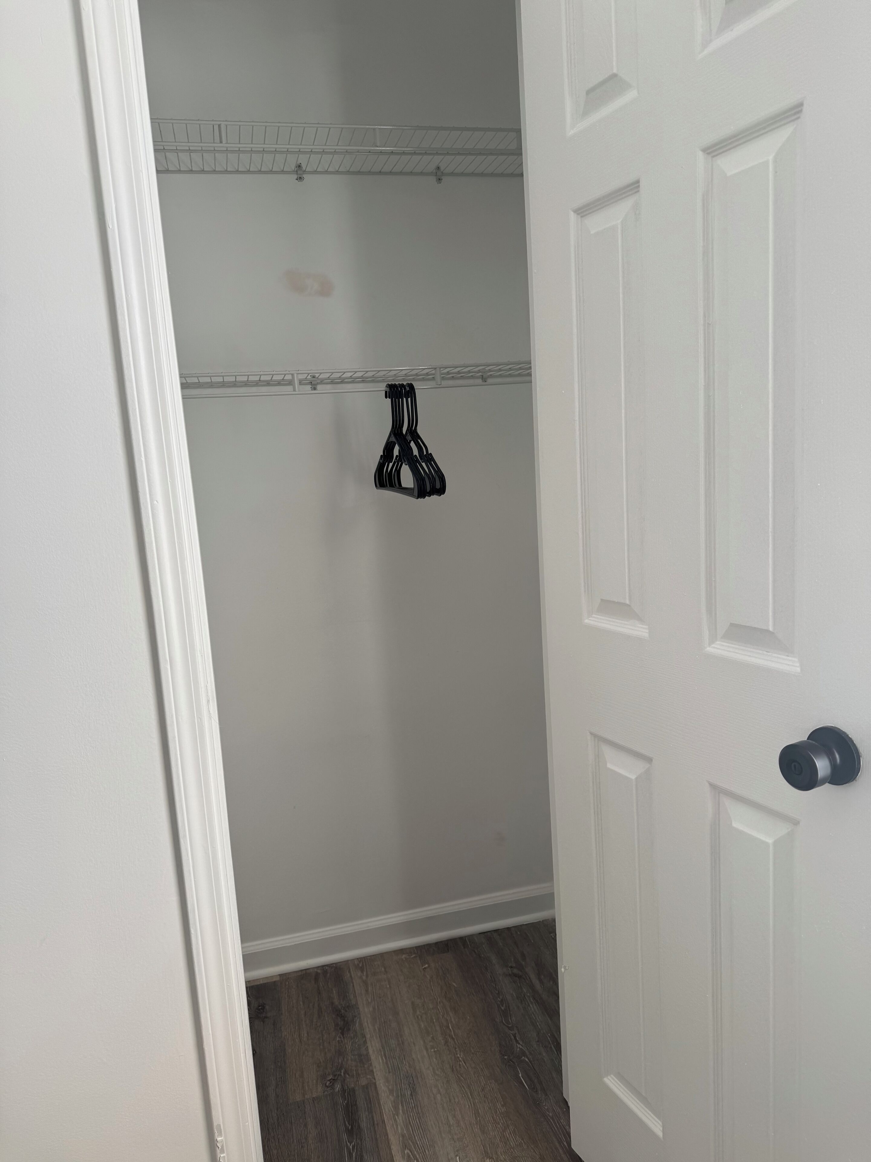 Un couloir avec une porte blanche, un plancher en bois et un portant à vêtements avec des cintres.