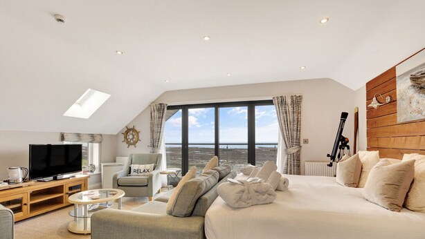 A modern hotel room with a large bed, a television, a cozy seating area, and a view of the sea. - Captains Cove at The Fishing Boat inn (Boulmer)
