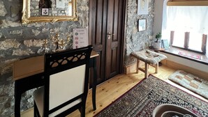 Une pièce avec un mur en pierre, un plafond en bois, une porte en bois, un banc, une table avec des chaises et une fenêtre donnant sur un paysage agréable.