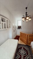 Un dormitorio con cama, cabecera de madera, alfombra estampada, estante montado en la pared y lámpara colgante.