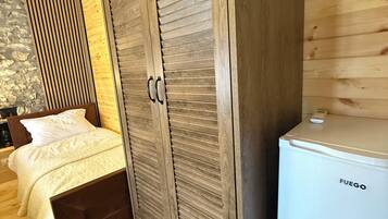A bedroom with a wooden wardrobe, a bed with white bedding, and a white Fuego refrigerator.