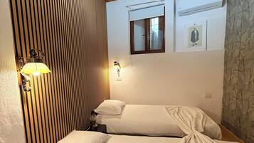Un dormitorio con dos camas, techo de madera, aire acondicionado de pared y una ventana pequeña con un cuadro.