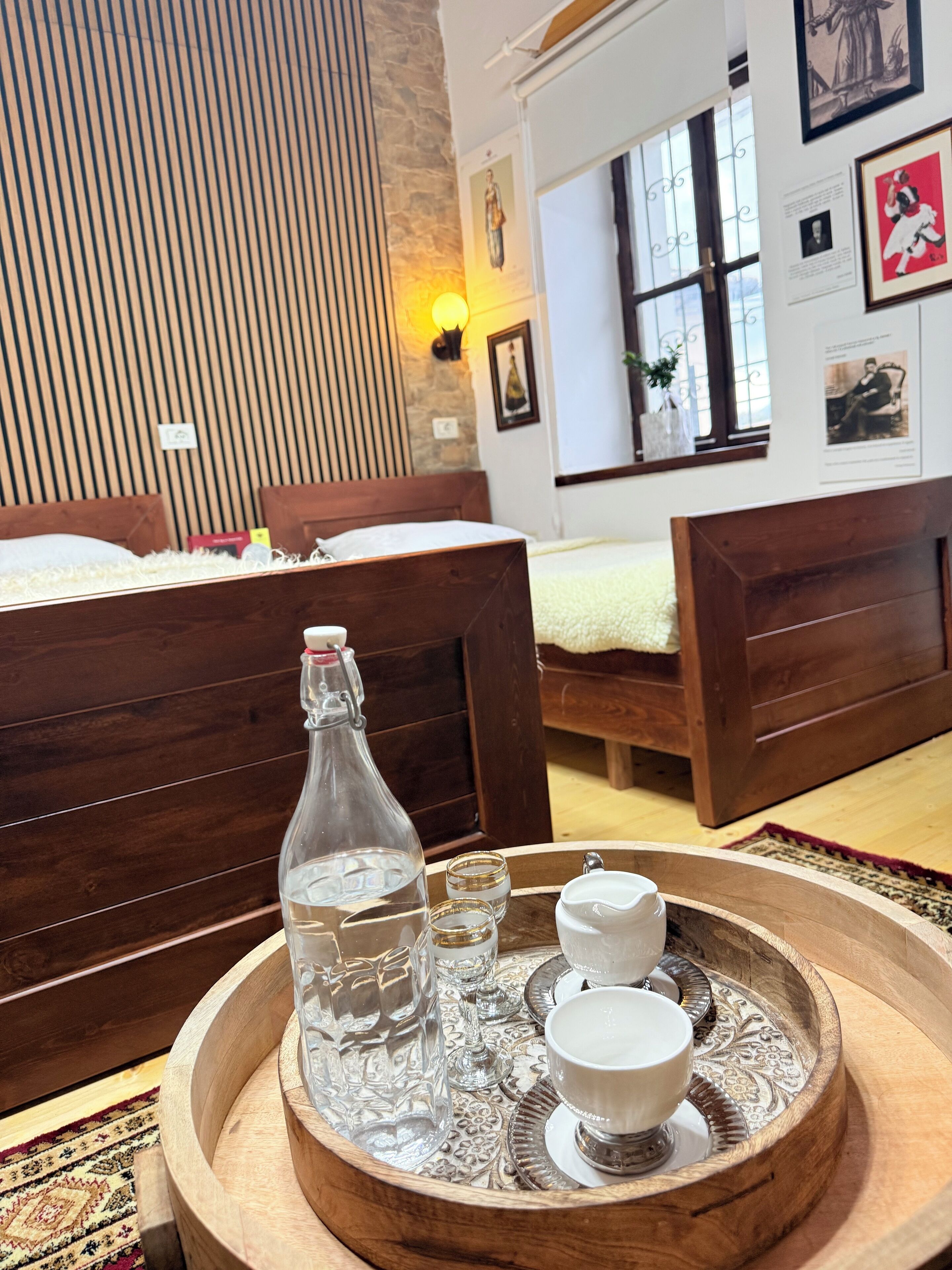 Ein Schlafzimmer mit zwei hölzernen Betten, einem Holftablett mit einer Flasche und Gläsern sowie einem Fenster mit Kunstwerk.