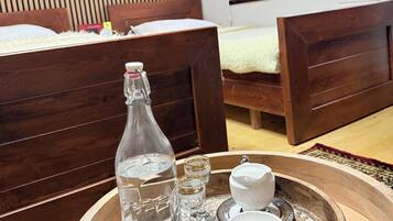 A bedroom with two wooden beds, a wooden tray with a bottle and glasses, and a window with artwork.