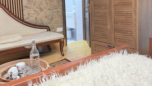 Une pièce avec un mur en pierre, un meuble en bois, un canapé et une petite table sur laquelle se trouvent une bouteille et des tasses.
