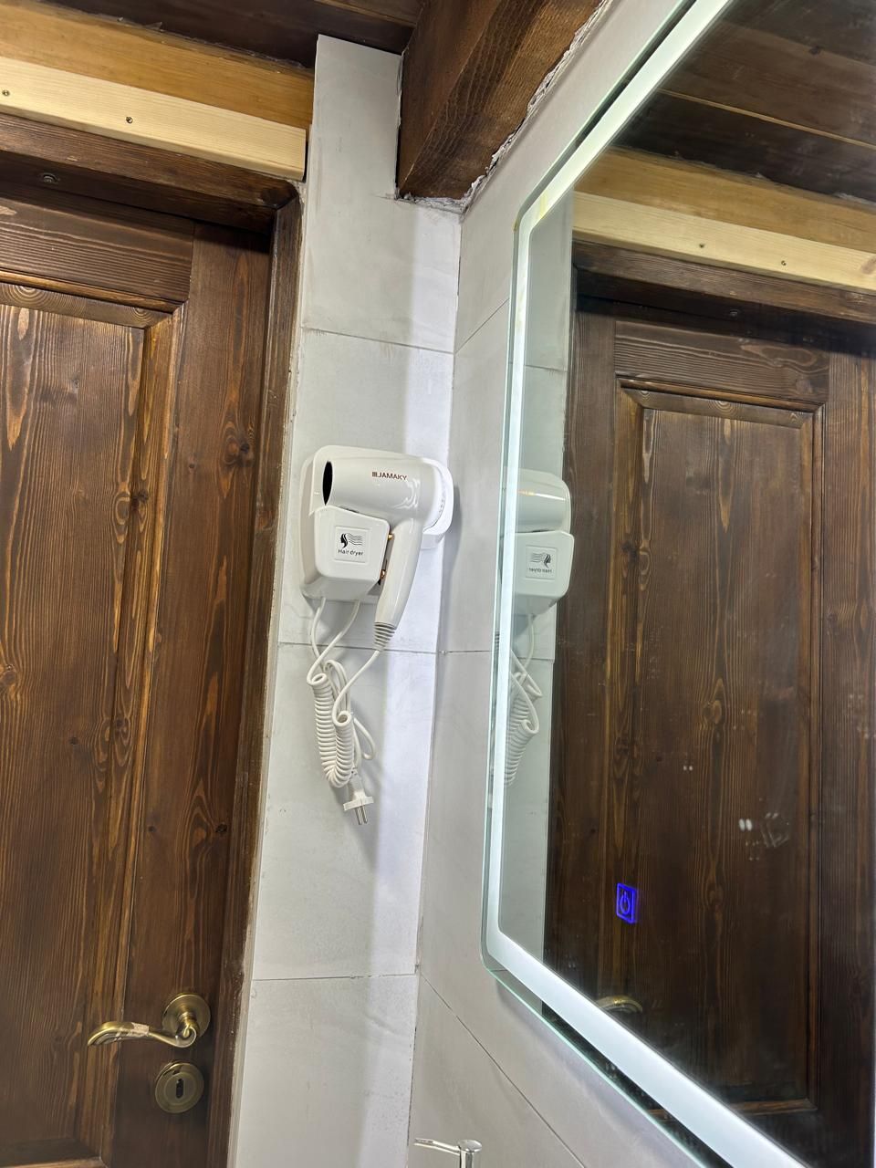 A room with a wooden door, a white wall-mounted hair dryer, and a large mirror.