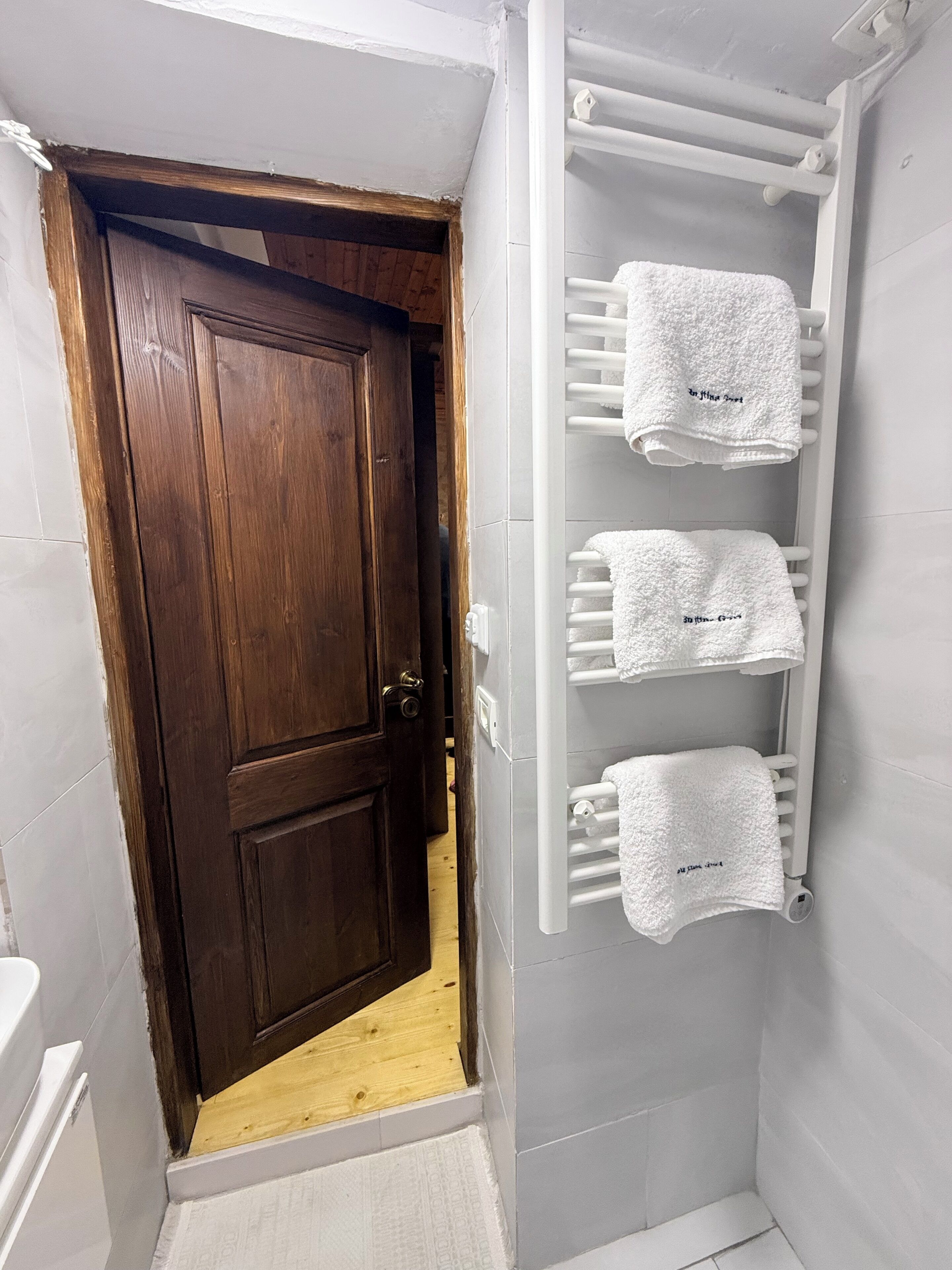 Un baño con puerta de madera, un toallero blanco con tres toallas y una bañera blanca.
