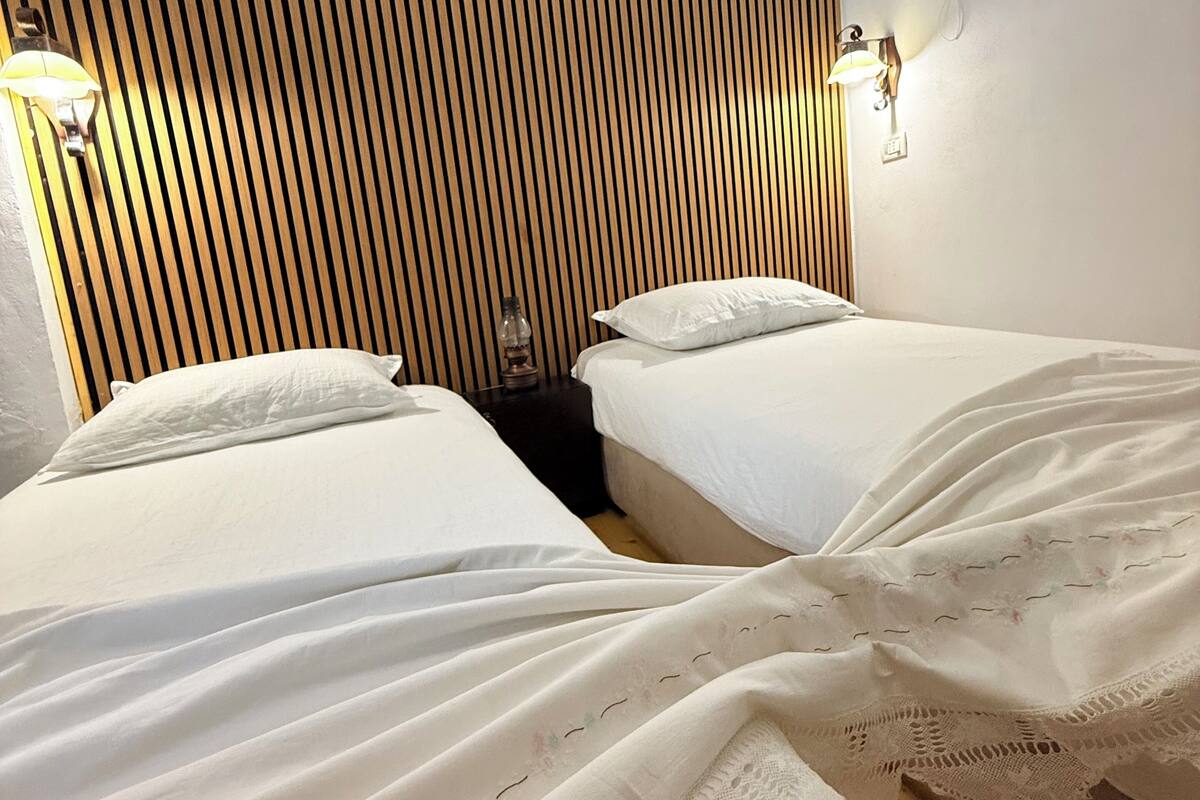 Een hotelkamer met twee bedden, een hoofdeinde van houten latten en wandlampen.