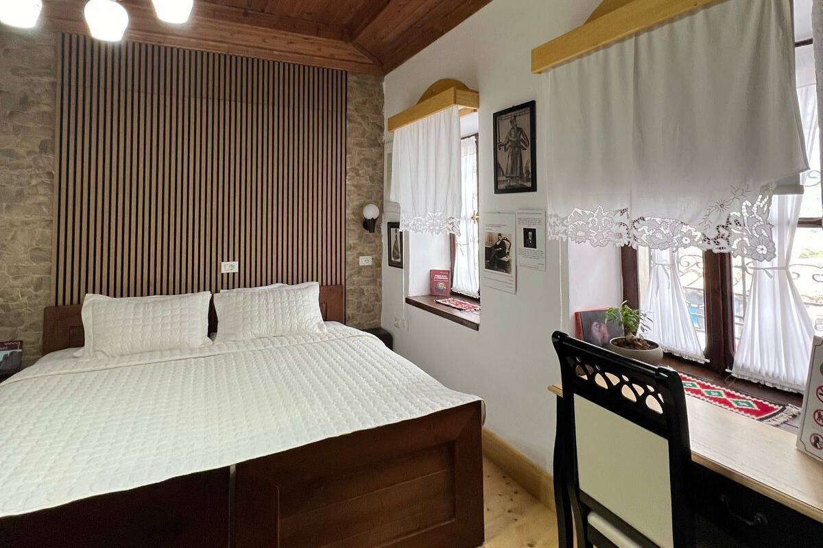 Een slaapkamer met een houten plafond, een bed met witte beddengoed, een bureau met stoel en een raam met gordijnen.