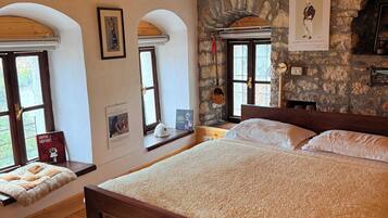 Un dormitorio con cama de madera, paredes de piedra y ventanas arqueadas.