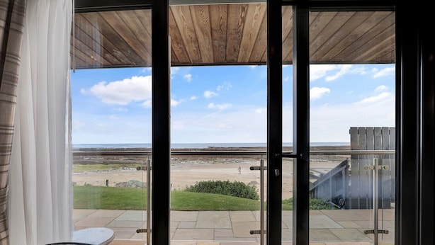 Una puerta de cristal da a un patio con vistas a la playa y una terraza de madera.