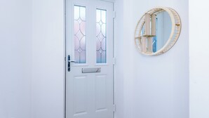 A white door with a glass panel and a mail slot, a round mirror on the wall, and a wooden floor. - 3 Bed-sleeps 5-garden-parking (Liverpool)
