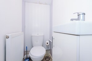 Une petite salle de bain blanche, équipée de toilettes, d’un radiateur et d’un lavabo.