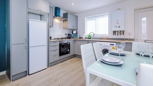 A modern kitchen with grey cabinets, a built-in oven, a dishwasher, and a dining area with a table set for four. - 3 Bed-sleeps 5-garden-parking (Liverpool)
