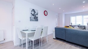 A modern living room with a grey sofa, a dining table with white chairs, and a wall clock. - 3 Bed-sleeps 5-garden-parking (Liverpool)