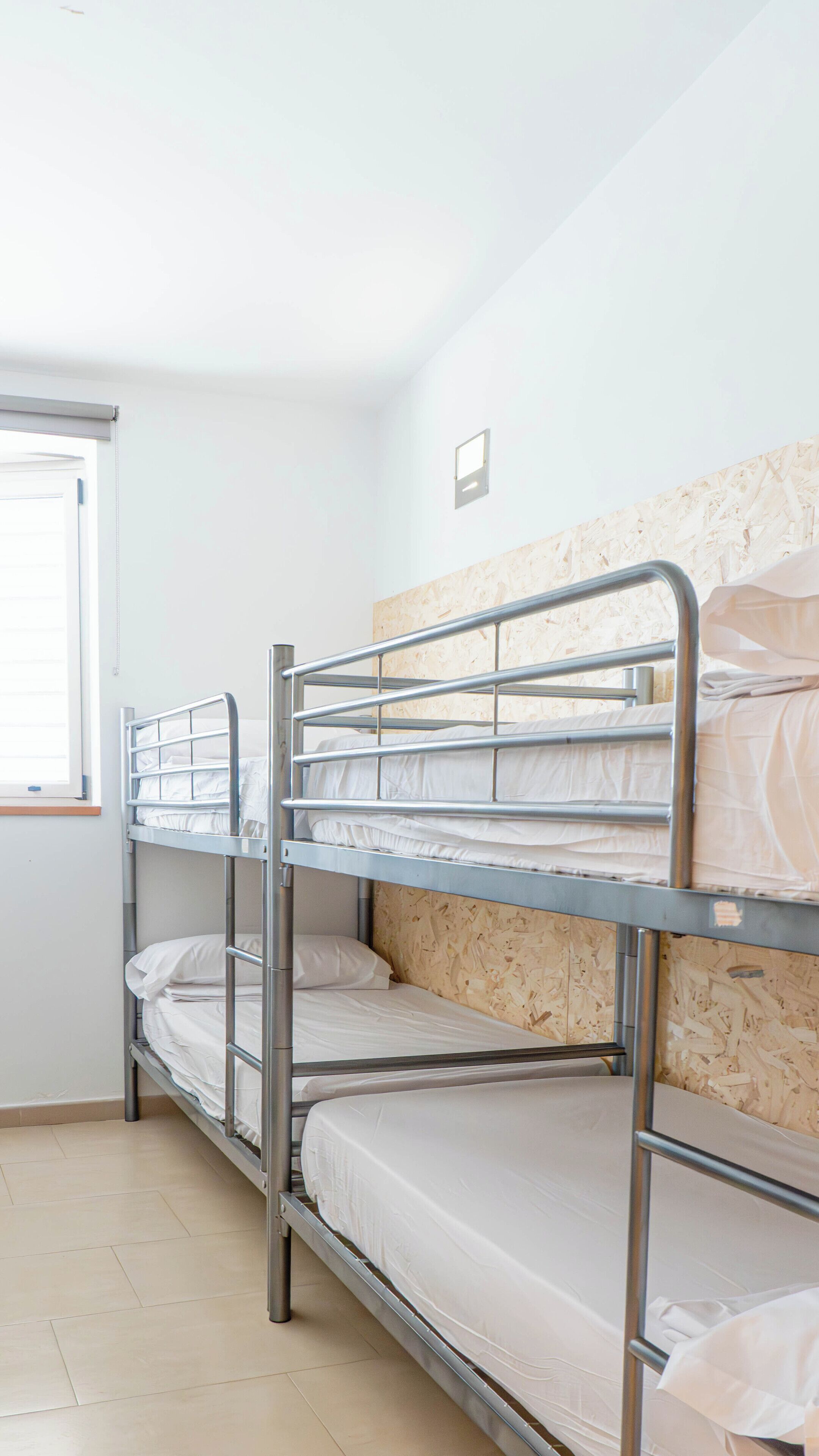 Une pièce avec des lits superposés, une fenêtre et un luminaire fixé au mur.
