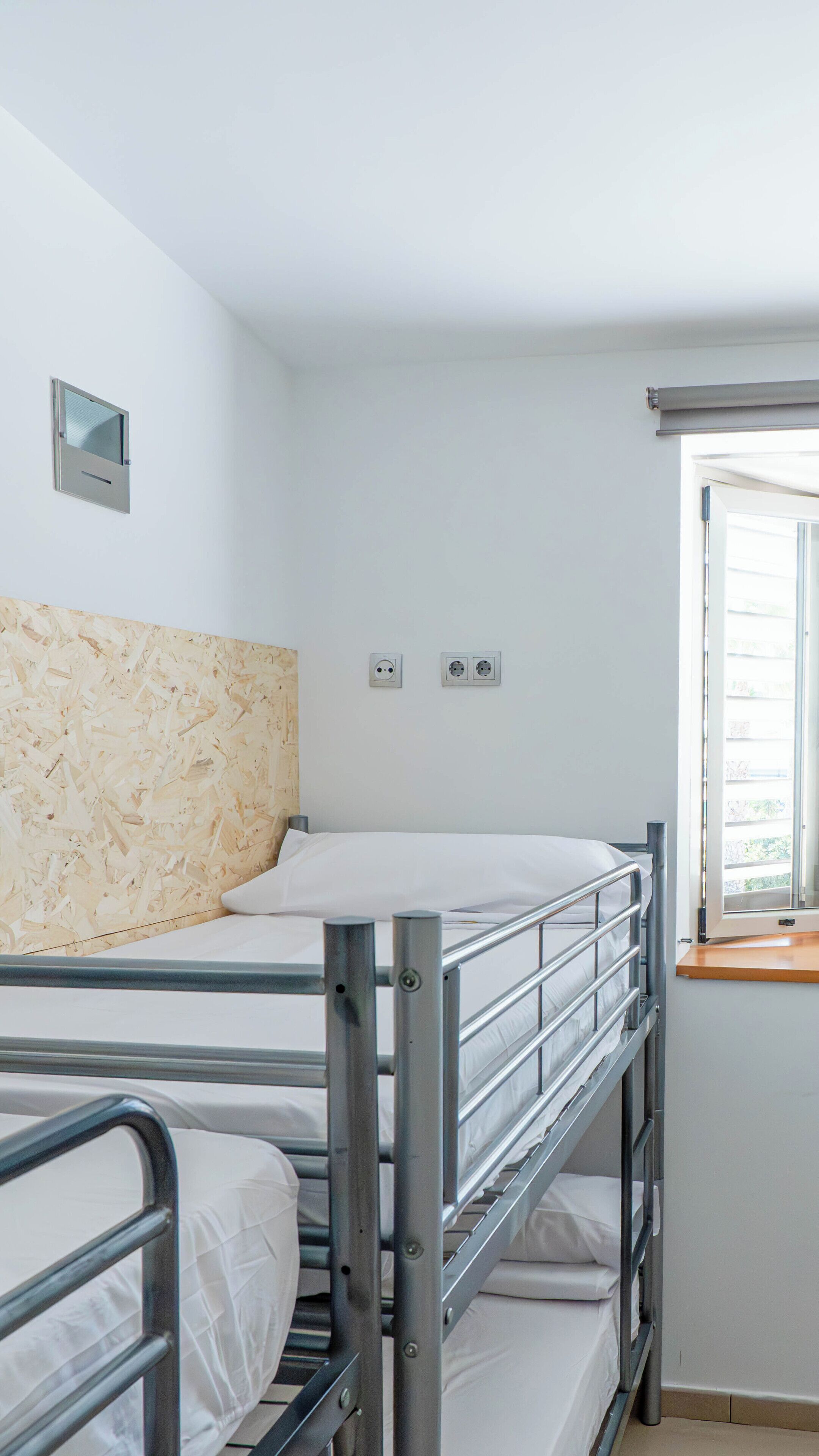 Habitación con literas, ventana, dos tomas de corriente e iluminación empotrada en la pared.
