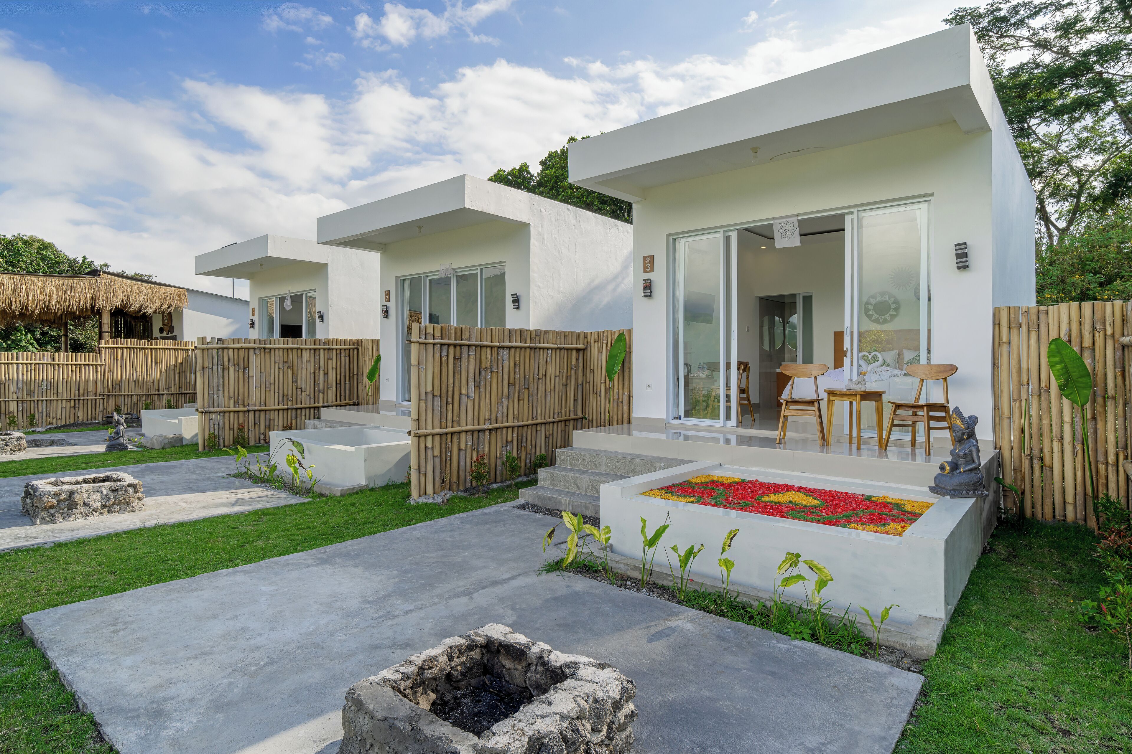 A modern, white building with a patio area, a stone fire pit, and a wooden fence.