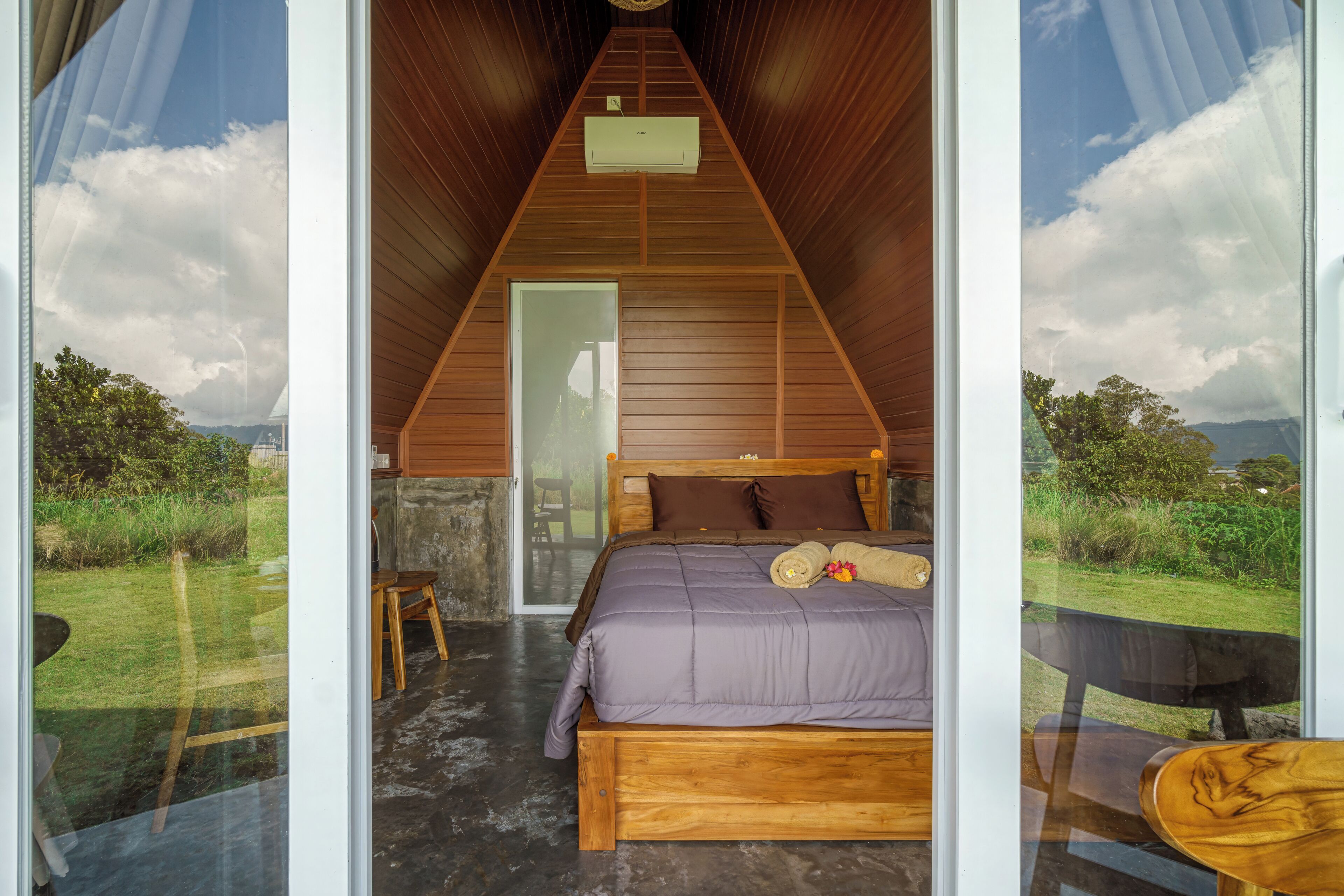 Une chambre avec un plafond en bois, un lit recouvert d’une courtepointe violette et une vue sur l’extérieur.