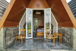 A triangular attic bedroom with a bed, two chairs, and a table. - PANDAWA GLAMPING KINTAMANI (Kintamani)