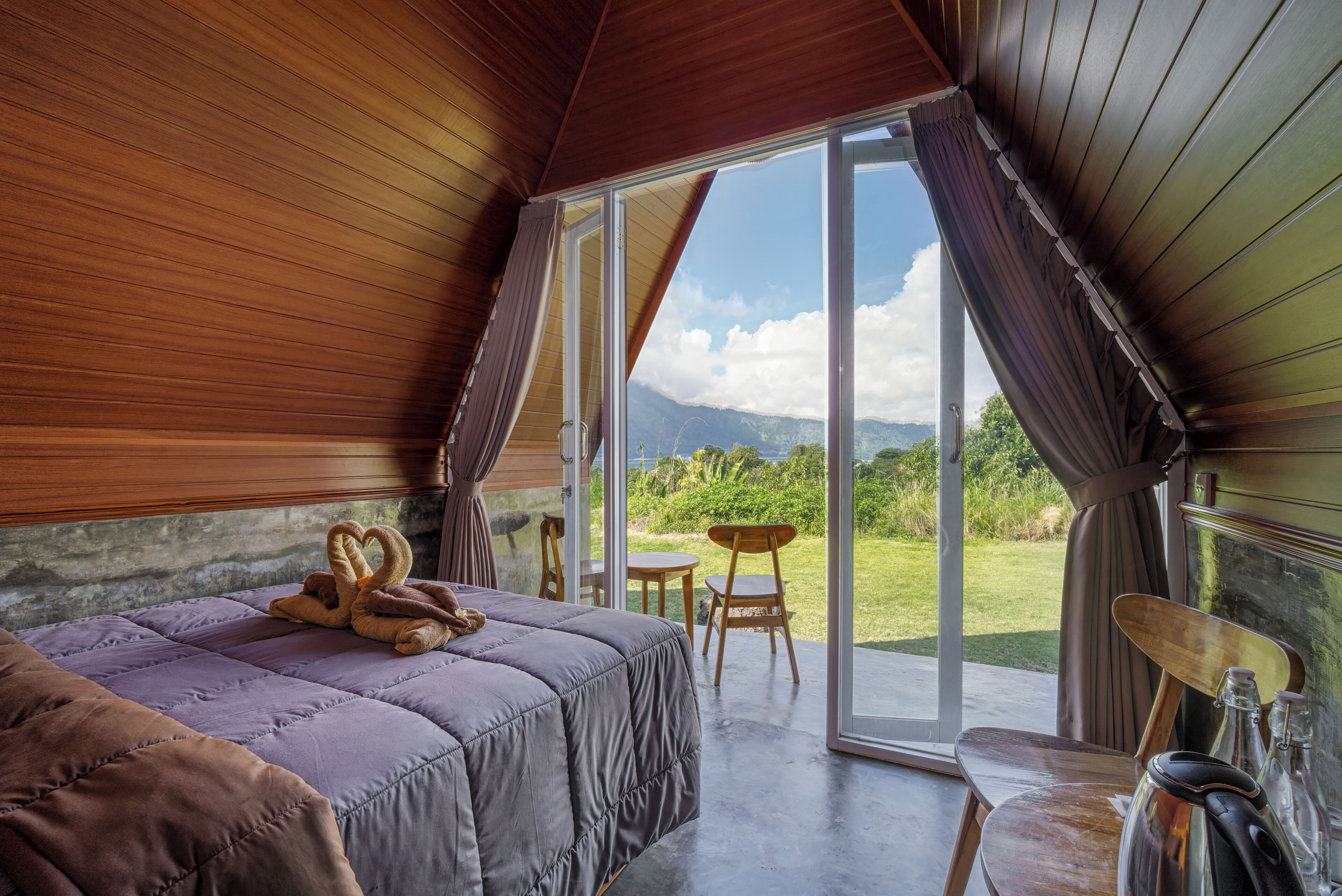 A bedroom with a bed, a table, chairs, and a view of the outdoors.