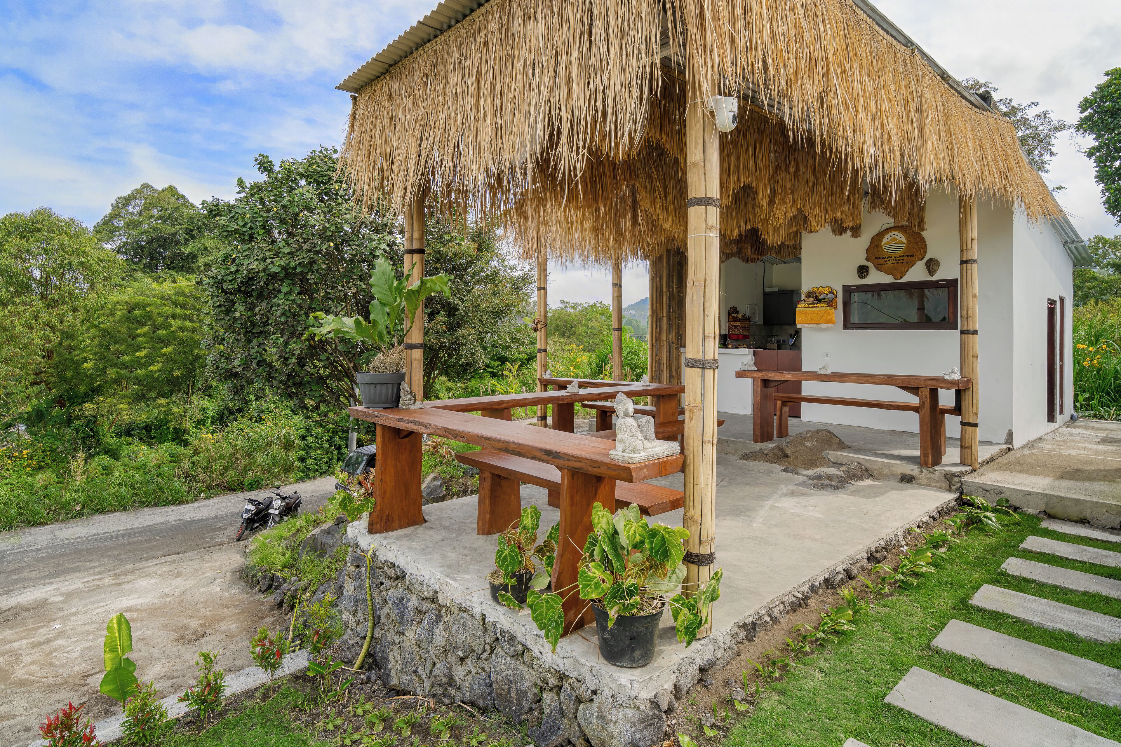 A thatched-roof structure with a concrete floor, wooden benches, and potted plants.