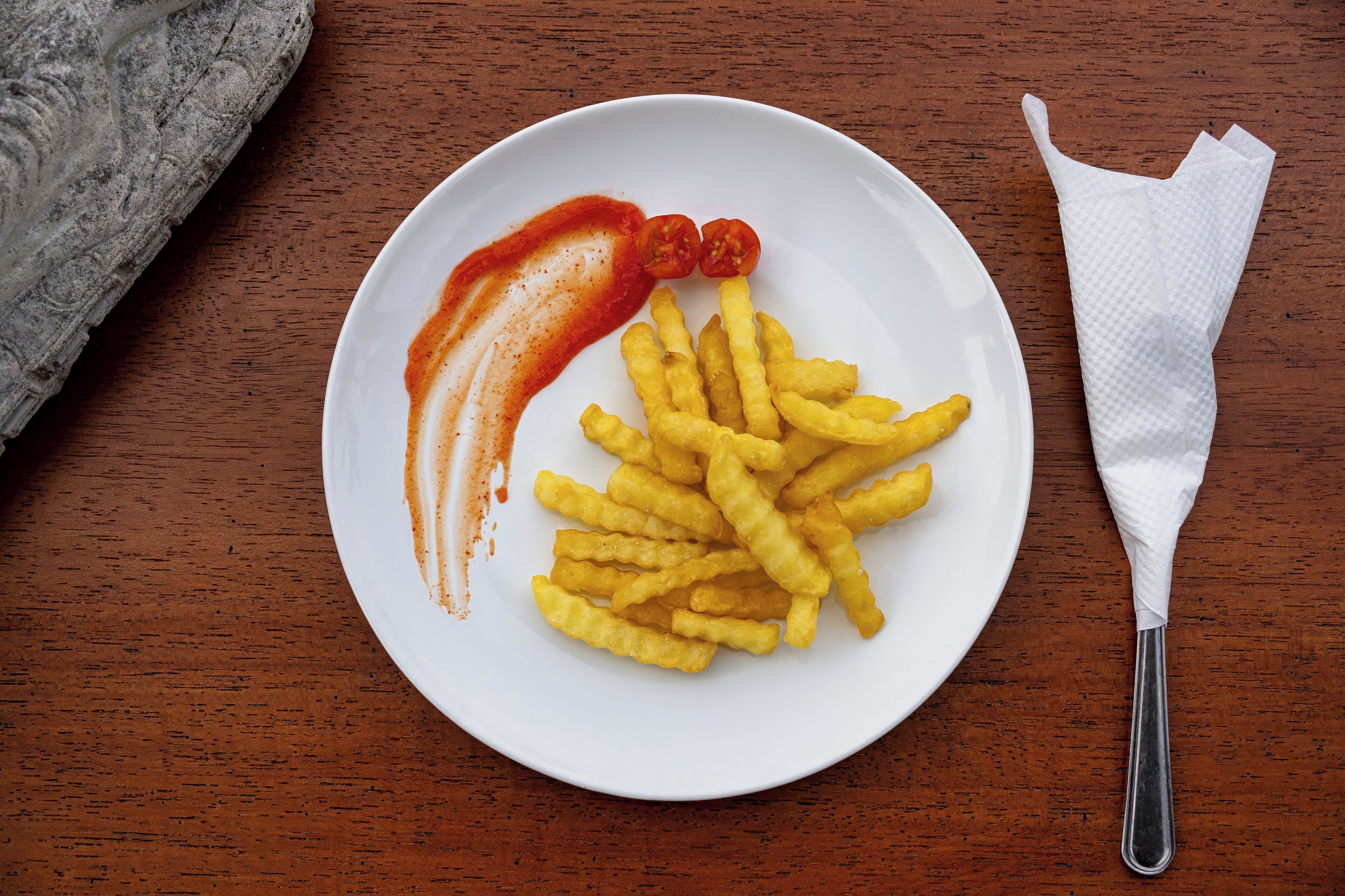 Un plato de papas fritas con kétchup y dos tomates cherry sobre una mesa de madera.