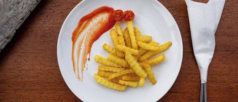 Un plato de papas fritas con kétchup y dos tomates cherry sobre una mesa de madera.