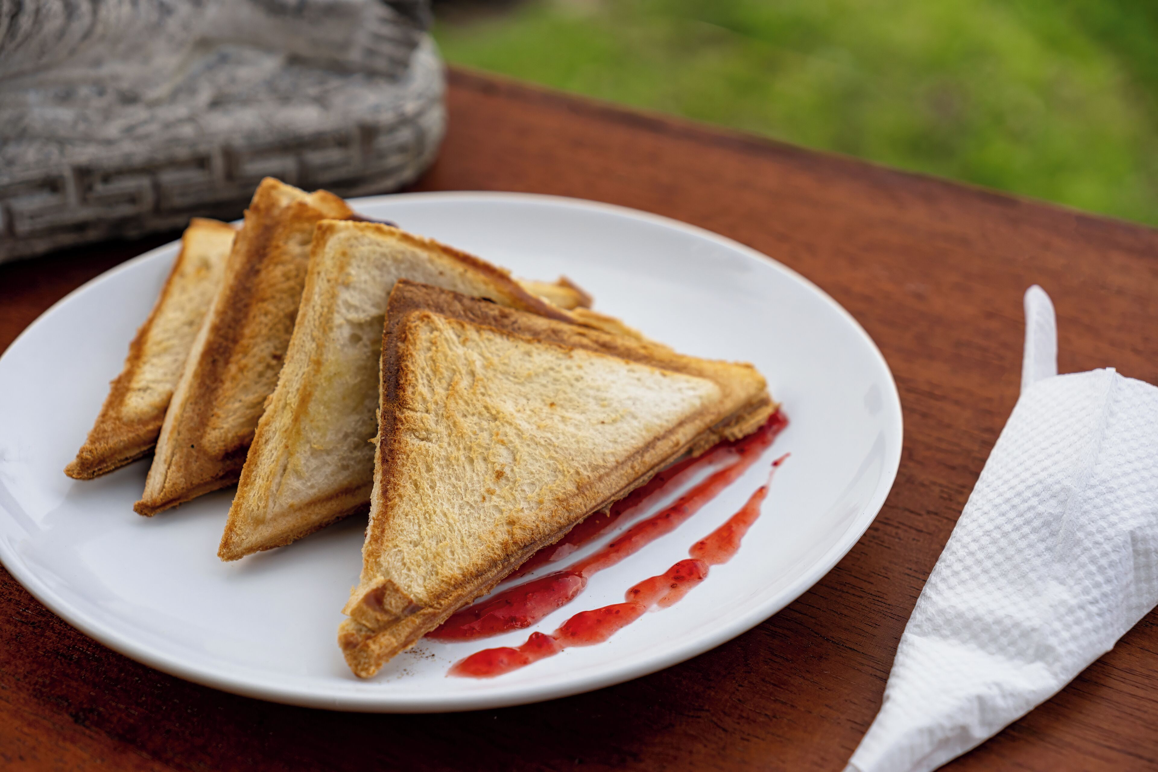 A plate with three triangular sandwiches and a white napkin on a wooden table.