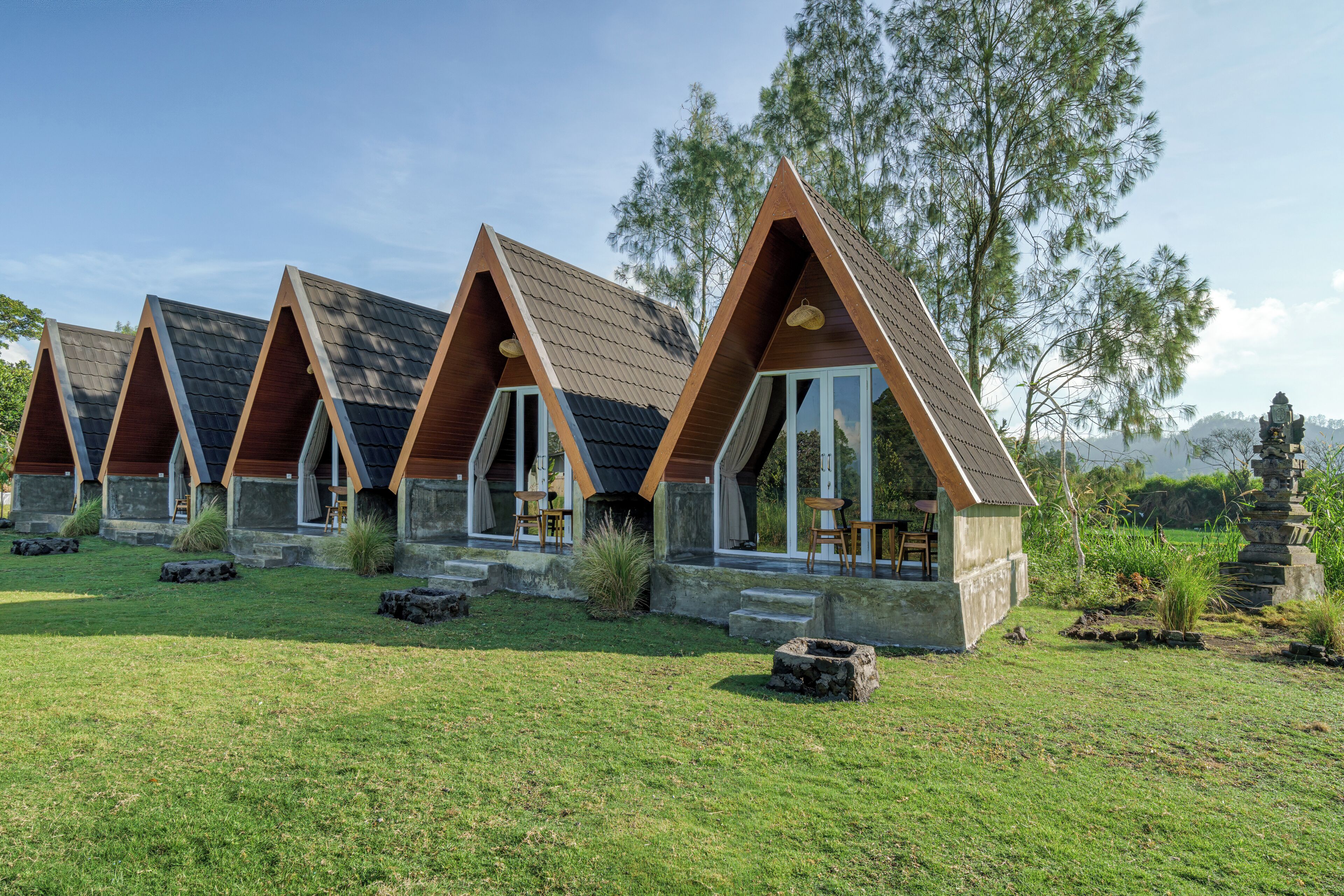 Een rij huisjes met puntige daken en stenen trappen naar de ingang, omgeven door gras en bomen.