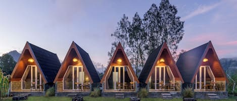 Une rangée de cabanes au toit triangulaire, dotées de grandes fenêtres et bordées d’une pelouse verdoyante.