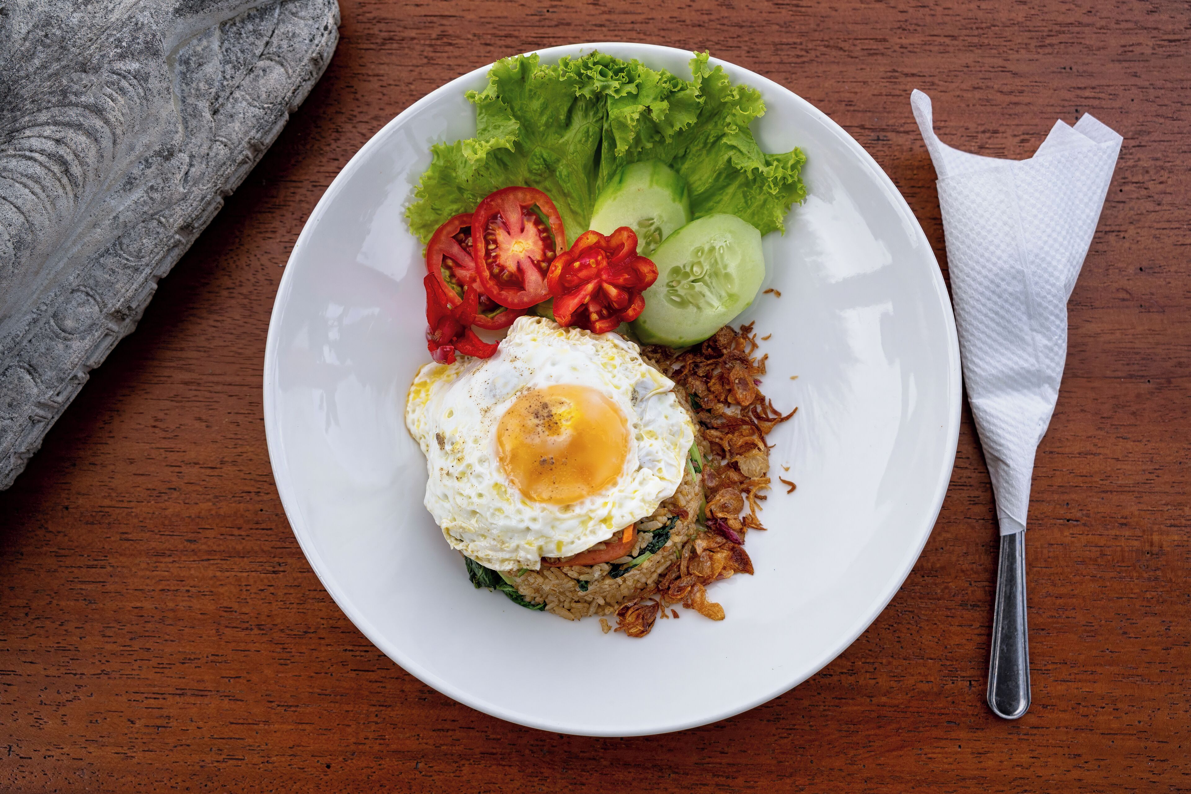 A plate of fried rice with vegetables and a fried egg on a wooden table.