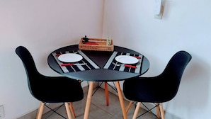 Un área de comedor con una mesa redonda, dos sillas negras y una pequeña cesta tejida.