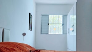 Un dormitorio con cama, armario, ventana con persianas y una lámpara de noche.